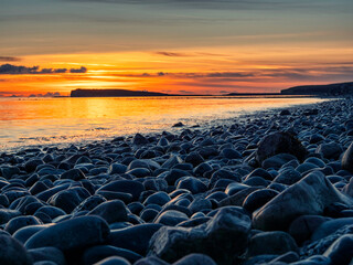 Obraz premium Colorful sunset over ocean, rough stone coast in foreground. Warm and cool color. Salthill beach, Galway city, Ireland. Selective focus. Nature scene with rich orange and blue color.