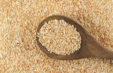 Chopped dry garlic pile in wooden spoon texture and background, top view