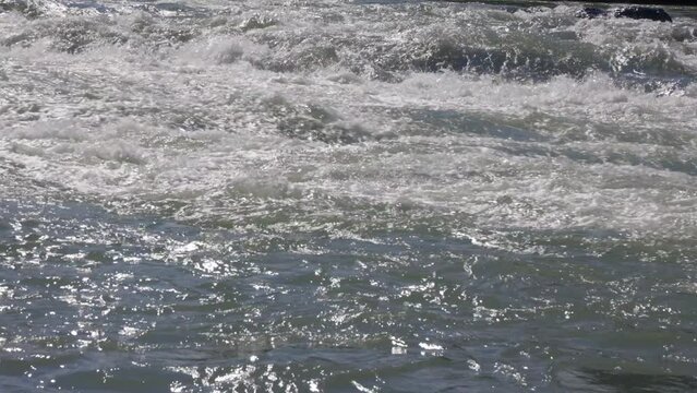 Streams of the Cold Mountain River noisily descend downstream through the rapids. Clear clear water in a deep mountain river flows in a narrow valley with steep banks and a rocky channel