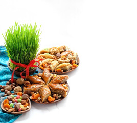 Obraz na płótnie Canvas Nowruz festive table. green wheat grass, arabic dessert baklava, sweets, nuts, dry fruits. on white background. Traditional celebration of spring equinox in March, Nowruz Holiday. copy space