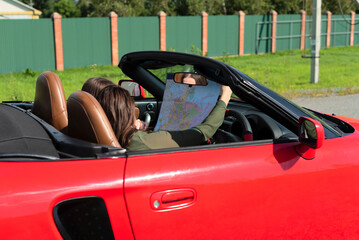 Happy girls driving red cabriolet car during vacation road trip having fun together discovering new places looking to the map. Road trip travel enjoying freedom concept. Selective focus