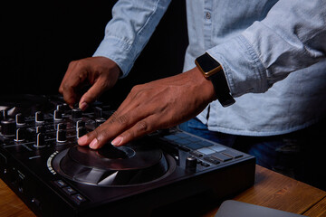 Professional dj console close up. Strong male hands of a dark-skinned man play music. The face is...