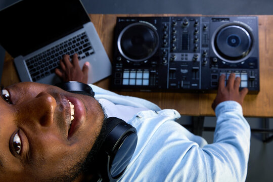 Dark skinned man with kind eyes raised his head and looked up at the camera to the photographer. A smiling African American man confidently plays modern music at the DJ console in the club - Powered by Adobe