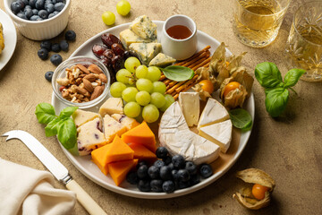Cheese board with fruits, nuts and snacks. Warm background.