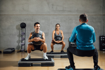 Sporty man and woman doing squats with fitness ball in the gym.