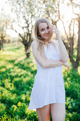 blonde woman in white dress walks in park flowering trees garden