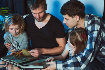 Staged photo. Homosexual couple and their children, two cute girls, at home.   All are excitedly...