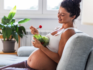 Pregnant woman eating salad on couch - obrazy, fototapety, plakaty