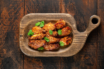 Pieces of fried chicken meat in barbecue sauce with parsley and crackers on a wooden board. Chicken Wings BBQ dish, top view