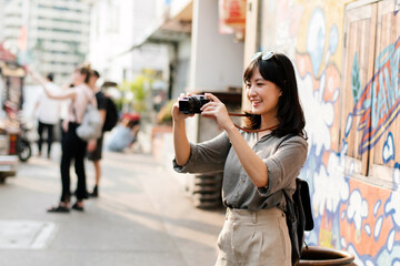 Young Asian woman backpack traveler using digital compact camera, enjoying street cultural local place and smile. Traveler checking out side streets.