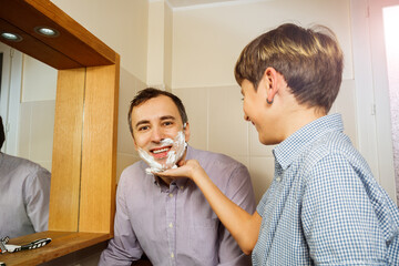 Smiling son touch father face to foam before shaving