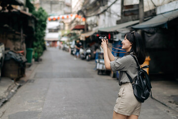 Young Asian woman backpack traveler using digital compact camera, enjoying street cultural local place and smile. Traveler checking out side streets.