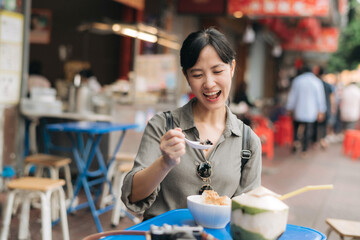 Happy young Asian woman backpack traveler enjoying street food at China town street food market in Bangkok, Thailand. Traveler checking out side streets.