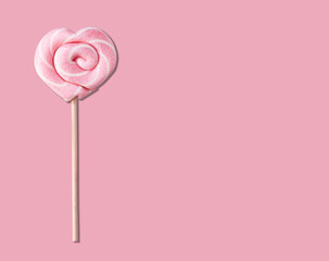 Pink lollipop in the form of a heart on a stick on a pastel pink background.