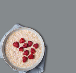 Oatmeal porridge with raspberries in a bowl on a gray isolated background. The concept of a dietary, healthy and nutritious breakfast.