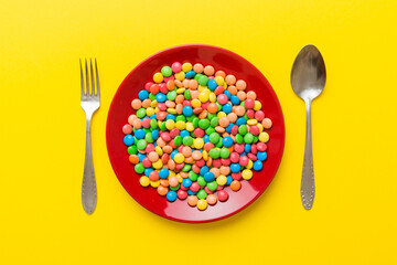 cutlery on table and sweet plate of candy. Health and obesity concept, top view on colored...