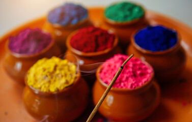 Burning and fuming aroma stick against circle of Holi powder in clay cups. Happy Holi greeting card and background