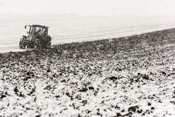 Late ploughing at the end of November in heavy snowfall. Tractor plowing.