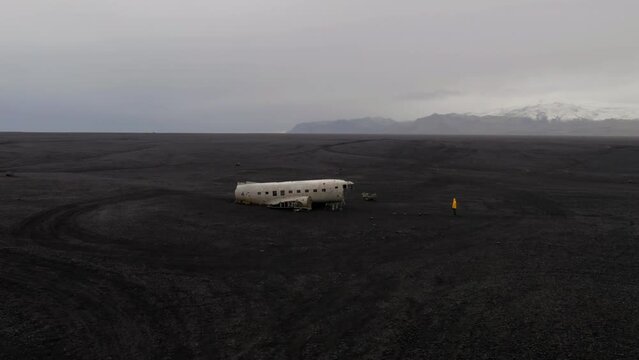 Drone orbit shot of one person standing in front of DC3 plane wreck in Iceland on a cloudy day