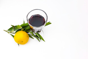 A glass of red wine with a ripe tangerine on a branch on a white background
