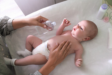 Mother massaging her baby with oil on changing table indoors, above view