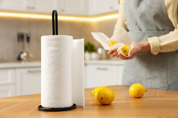 Woman wiping lemons with paper towels in kitchen, closeup, focus on table