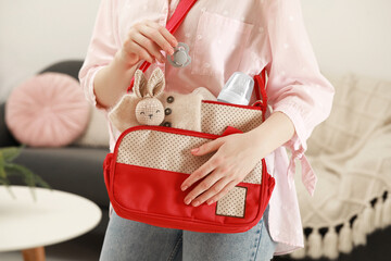 Woman putting pacifier into mother`s bag indoors, closeup
