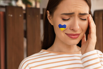 Sad young woman with drawing of Ukrainian flag on face outdoors, closeup. Space for text