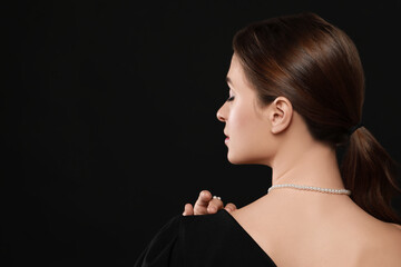 Young woman wearing elegant pearl jewelry on black background, back view. Space for text