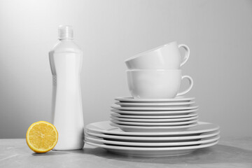 Set of clean tableware, dish detergent and lemon on grey table against light background