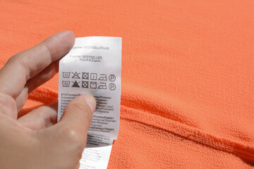 Woman holding clothing label on coral garment, closeup. Space for text