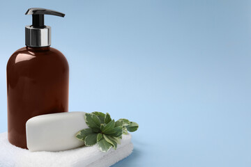 Soap bar, bottle dispenser and towel on light blue background, space for text