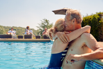 Loving Retired Senior Couple Hugging At Side Of Swimming Pool On Summer Vacation 