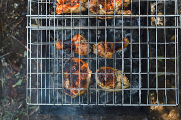 Outdoors, top view of a grill grate on which chicken meat with a golden crust is baked on charcoal and fire, copy space.
