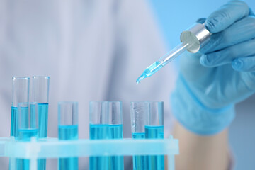 Scientist dripping liquid from pipette into test tube on blurred background, closeup
