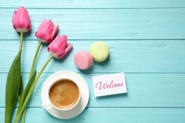 Welcome card, beautiful pink tulips, macarons and cup of coffee on light blue wooden table, flat lay