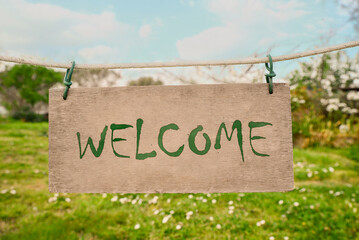 Welcome card. Wooden board with word hanging on rope in countryside
