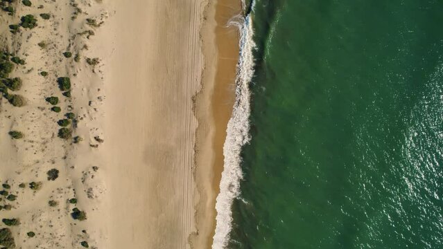 aerial rising view of the waves of the atlantic ocean rolling over the beach of huelva in spain