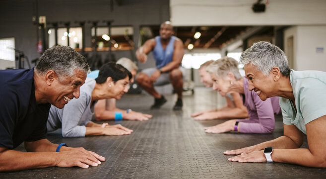 Senior people, fitness and plank with personal trainer in class for workout, core exercise or training at gym. Elderly group in coaching ab session for strong abdominal muscles on gymnasium floor