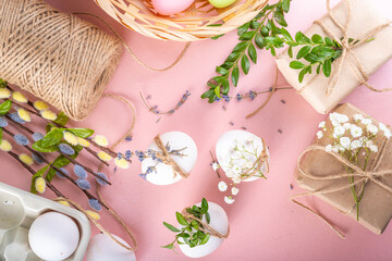 Fototapeta na wymiar Eco friendly zero waste Easter flatlay. Spring flowers, leaves, eggs on pink pastel background, with craft paper gift box. Woman hands decorate eggs with organic natural decor, preparation for Easter