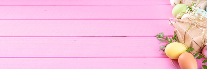 Pink Easter greeting card background with spring flowers, green leaf branches and colorful pastel Easter eggs, top view copy space