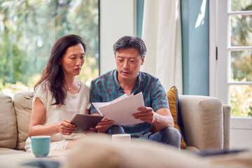Mature Couple Sitting On Sofa At Home Reviewing Personal Finances On Laptop