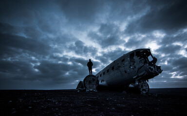 Image of the downed and abandoned plane in Sólheimasandur, Iceland, with a person standing on top enjoying the black sand landscape.