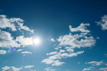 The blue summer sky with white fluffy clouds. Shining sun at clear blue sky with copy space