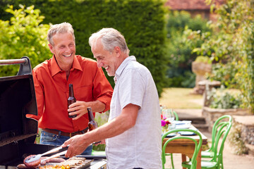 Two Senior Male Friends Cooking Outdoor Barbeque And Drinking Beer At Home Together
