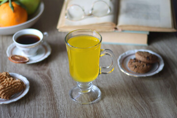 Cup of tea, plates with cookies, glass of orange juice, books, reading glasses, bowl of fruit and candles on the table. Selective focus.