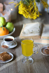 Cup of tea, plates with cookies, glass of orange juice, books, reading glasses, bowl of fruit and candles on the table. Selective focus.