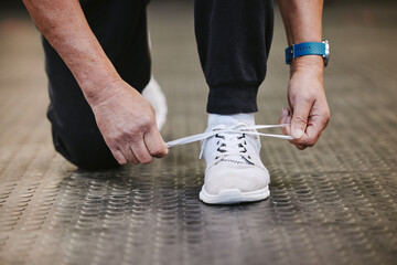 Fitness, tie shoes and hands in gym to start workout, training or exercise for wellness. Sports, athlete health and senior man tying sneakers or footwear laces to get ready for exercising or running.