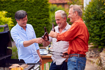 Three Senior Male Friends Cooking Outdoor Barbeque And Drinking Beer At Home Together