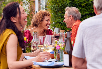 Group Of Mature Friends Talking Around Table At Summer Dinner Party In Garden At Home